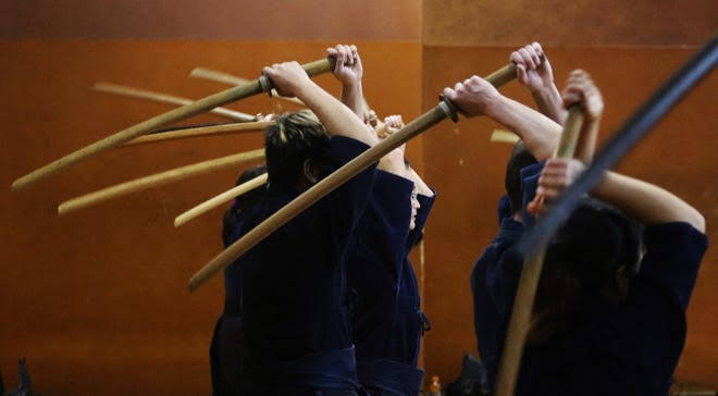 Kendoka performing synchronized suburi in a dojo — collective discipline and focused training