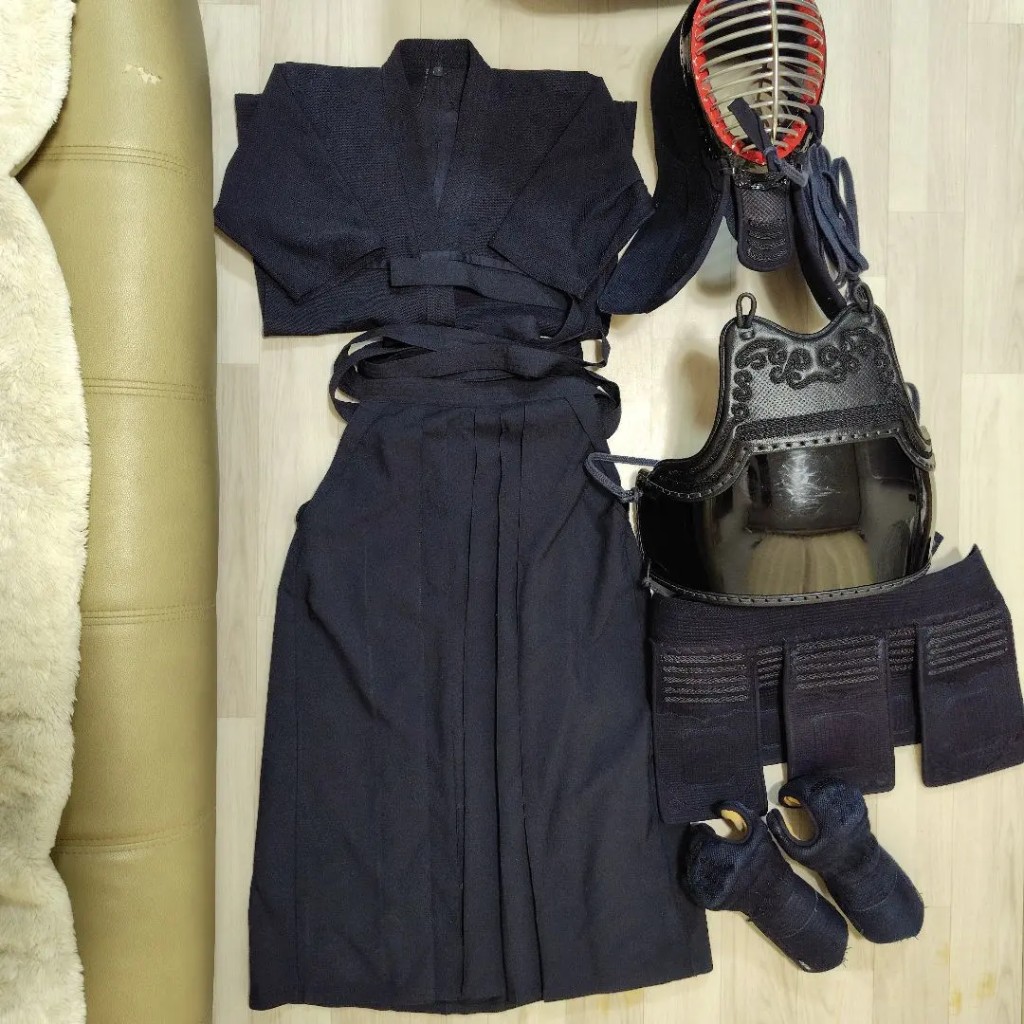 Complete kendo uniform and bogu laid out — kendogi, hakama, men, do, tare, and kote